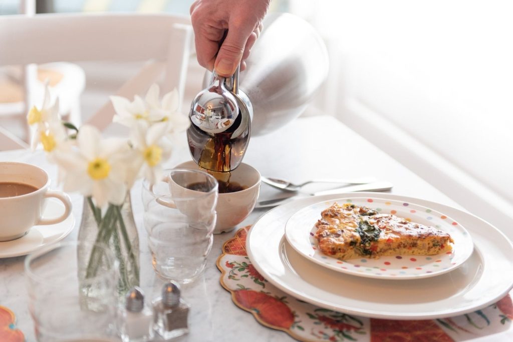 A person pouring syrup over a cake at a New England bed and breakfast breakfast setting.